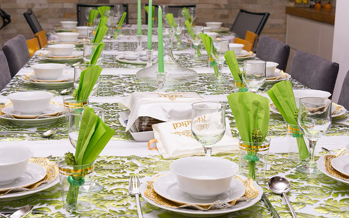 Modern Passover Seder table with green  and gold decorations in Tel Aviv, Israel, complete with Matzos and a traditional Seder Plate.  Matzo covers read "Matzo" and "Afikoman" in Hebrew.