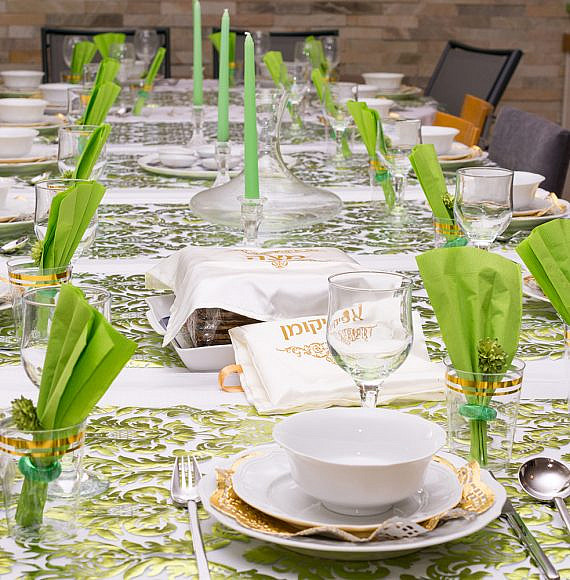 Modern Passover Seder table with green  and gold decorations in Tel Aviv, Israel, complete with Matzos and a traditional Seder Plate.  Matzo covers read "Matzo" and "Afikoman" in Hebrew.